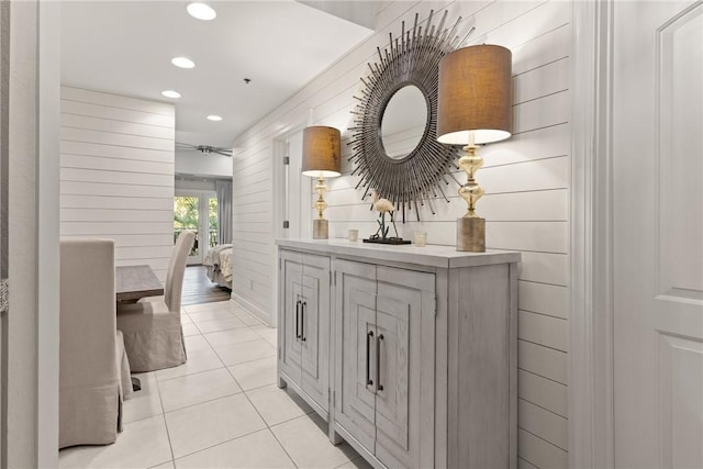 corridor with recessed lighting, light tile patterned flooring, and wood walls