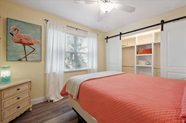 bedroom with a barn door, baseboards, dark wood-style flooring, and a ceiling fan