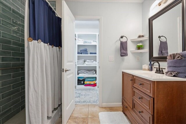 full bath featuring a tile shower, vanity, tile patterned floors, and baseboards