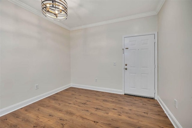 spare room with wood finished floors, a notable chandelier, ornamental molding, and baseboards