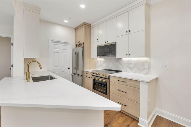 kitchen with appliances with stainless steel finishes, a peninsula, light wood-style flooring, decorative backsplash, and a sink
