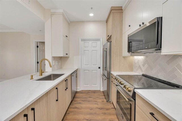 kitchen with a sink, light wood-style floors, light stone countertops, backsplash, and stainless steel appliances