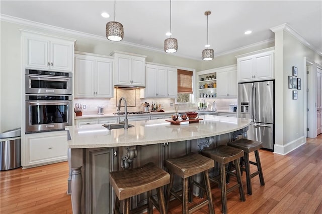 kitchen with white cabinets, light wood-type flooring, stainless steel appliances, and a kitchen island with sink