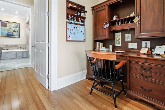 home office with ornamental molding, light wood-type flooring, and built in desk