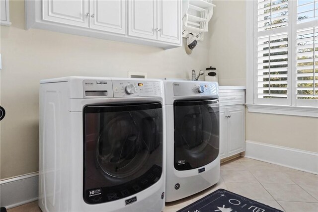 laundry room featuring washing machine and clothes dryer, a wealth of natural light, light tile patterned floors, and cabinets