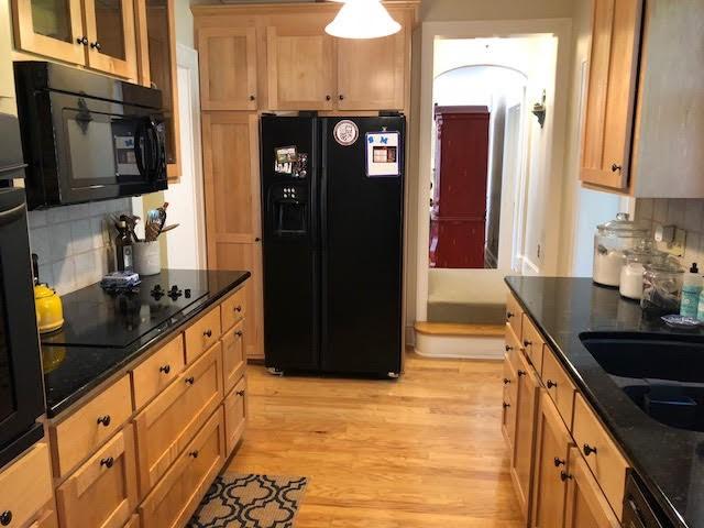 kitchen featuring decorative backsplash, black appliances, light wood-type flooring, and dark stone counters