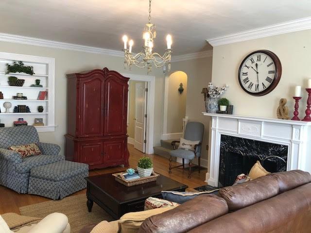 living area with crown molding, built in features, a fireplace, wood finished floors, and arched walkways