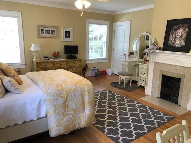 bedroom with crown molding, multiple windows, a fireplace, and wood finished floors