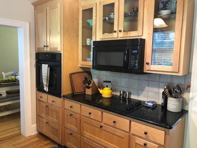 kitchen featuring light wood-style floors, black appliances, glass insert cabinets, and tasteful backsplash