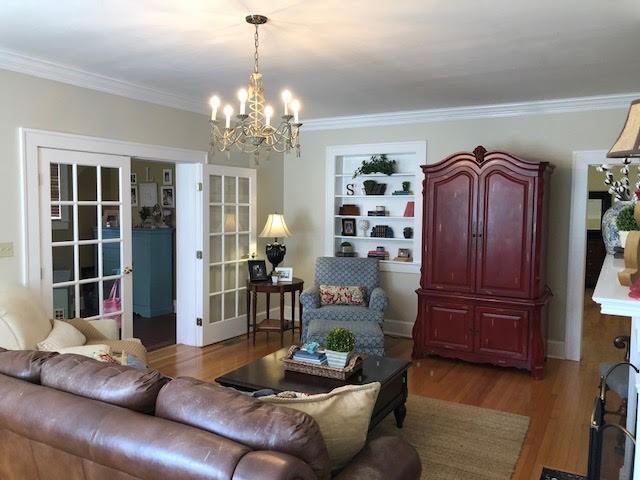 living area with crown molding, built in features, light wood-type flooring, and a chandelier