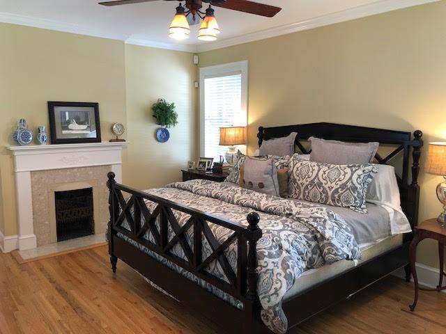 bedroom featuring ceiling fan, a high end fireplace, wood finished floors, and crown molding