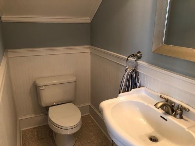 bathroom featuring a wainscoted wall, ornamental molding, toilet, and a sink