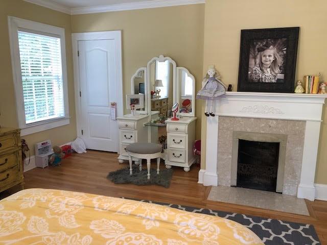 bedroom with a fireplace with flush hearth, wood finished floors, and ornamental molding