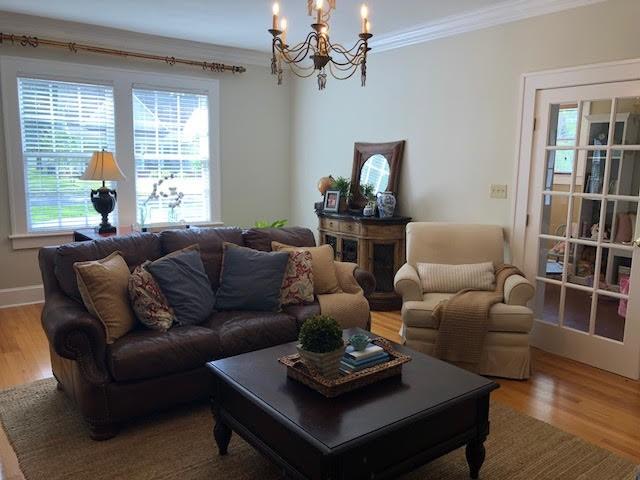 living area featuring baseboards, wood finished floors, a notable chandelier, and ornamental molding