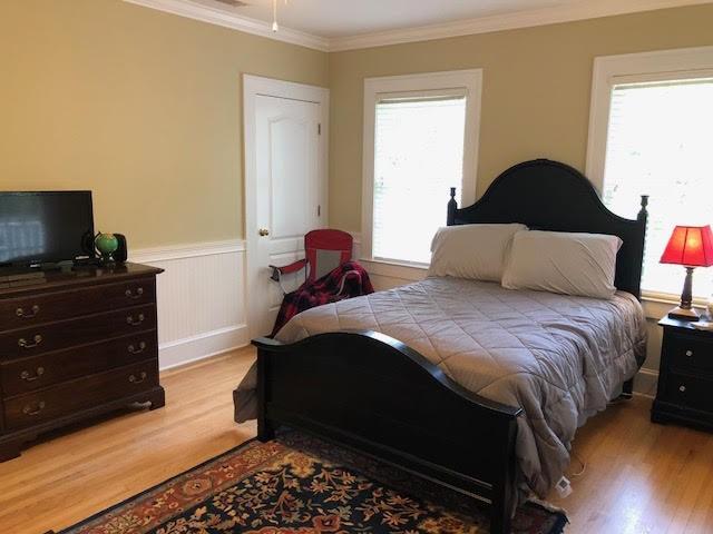 bedroom featuring wainscoting, wood finished floors, and ornamental molding