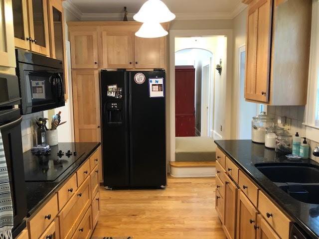 kitchen with light wood finished floors, black appliances, dark stone counters, and ornamental molding