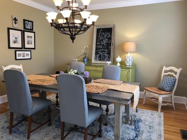 dining space with an inviting chandelier, crown molding, wood finished floors, and baseboards