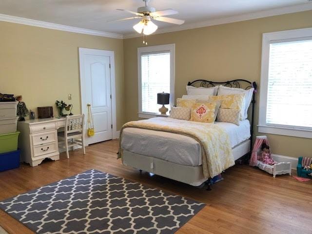 bedroom with baseboards, multiple windows, wood finished floors, and crown molding