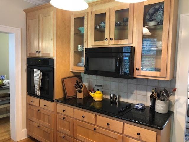 kitchen with dark stone countertops, decorative backsplash, glass insert cabinets, and black appliances