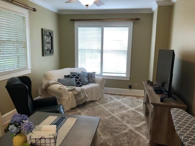 living area with baseboards, ceiling fan, and crown molding