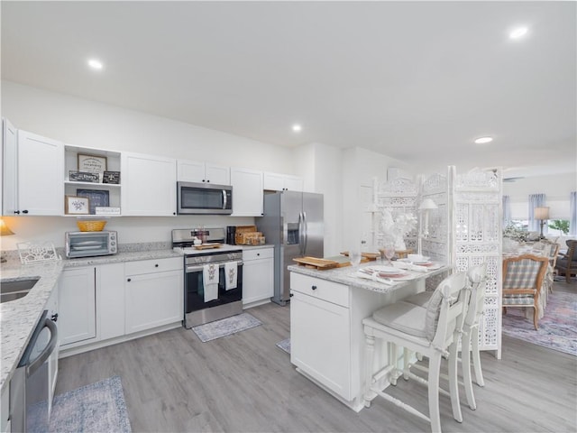 1007 Elbert Ext, Darien, GA 31305 - kitchen with stainless steel appliances, open shelves, a breakfast bar, light stone countertops, and white cabinetry