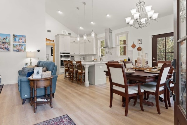 dining room with light wood finished floors, high vaulted ceiling, and a chandelier