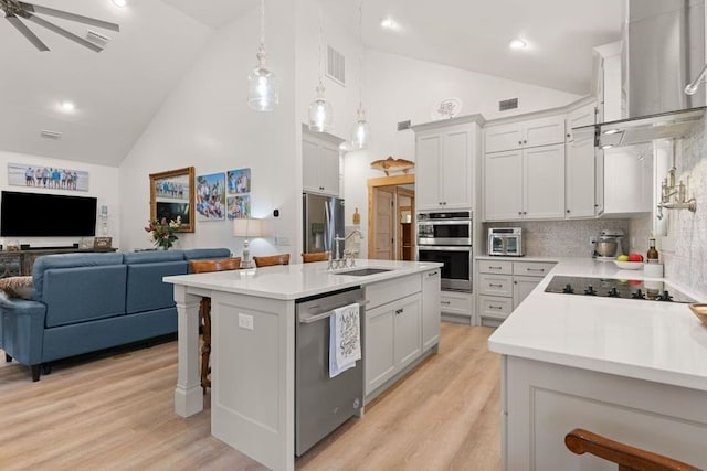 kitchen with a sink, visible vents, open floor plan, wall chimney range hood, and appliances with stainless steel finishes