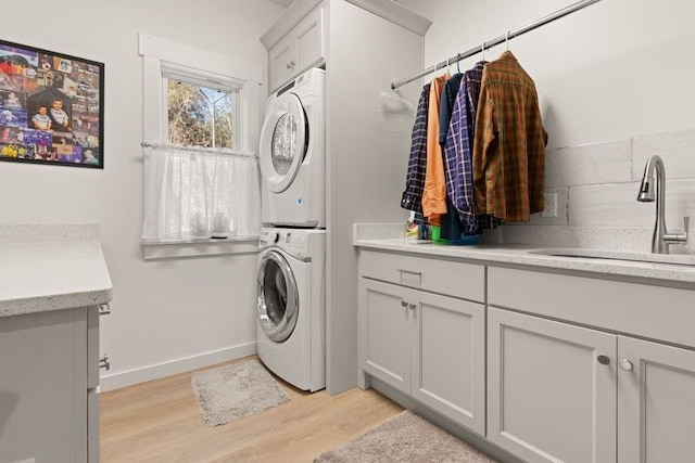 laundry area with baseboards, a sink, light wood-style flooring, and stacked washer / drying machine