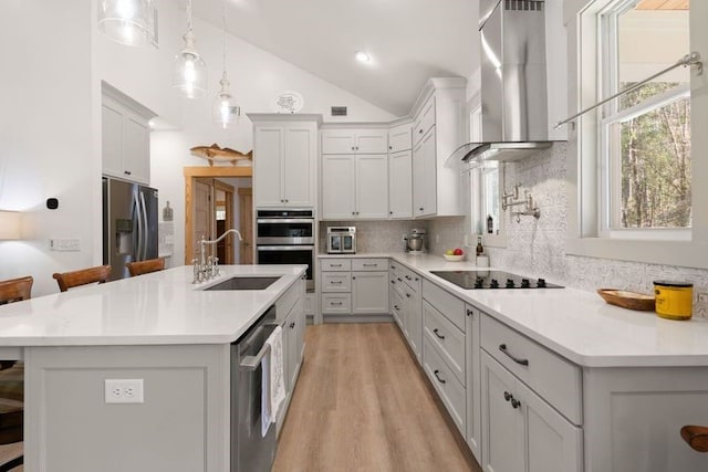 kitchen with stainless steel appliances, light countertops, vaulted ceiling, a sink, and wall chimney range hood