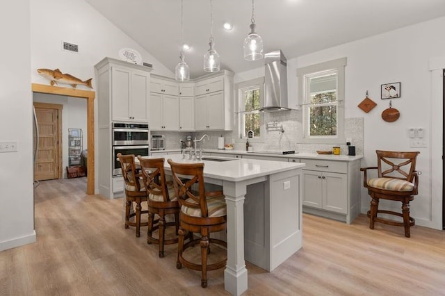 kitchen featuring black electric stovetop, light countertops, decorative backsplash, double oven, and wall chimney range hood