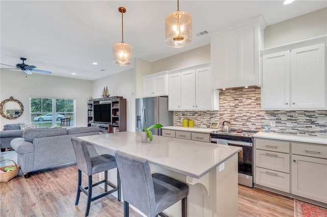 kitchen with a breakfast bar area, white cabinets, decorative light fixtures, and appliances with stainless steel finishes