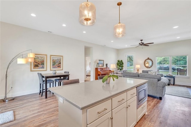 kitchen with stainless steel microwave, white cabinets, hanging light fixtures, ceiling fan, and light wood-type flooring