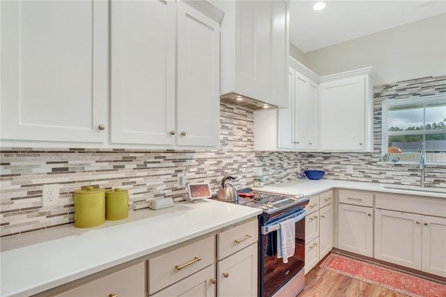 kitchen with electric range, sink, backsplash, white cabinets, and light wood-type flooring