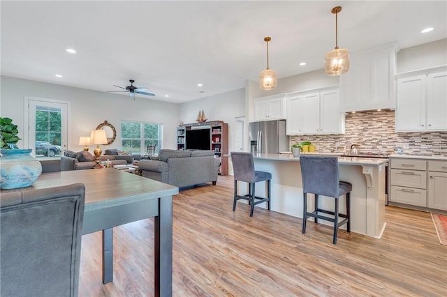 kitchen with a breakfast bar, a kitchen island with sink, white cabinets, hanging light fixtures, and stainless steel fridge