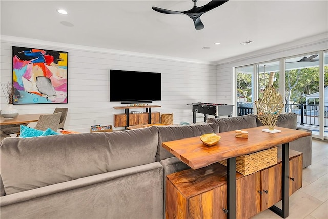 living room featuring light hardwood / wood-style flooring, ceiling fan, ornamental molding, and wood walls