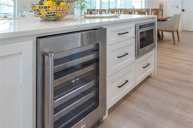 kitchen featuring light stone countertops, white cabinetry, beverage cooler, and light hardwood / wood-style flooring