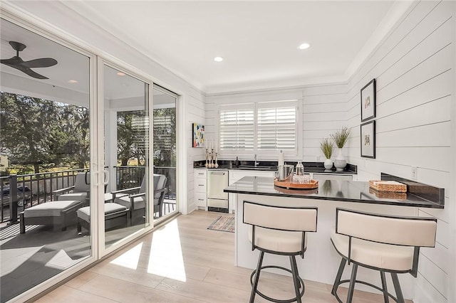 kitchen with white cabinets, sink, stainless steel dishwasher, light hardwood / wood-style floors, and a breakfast bar area