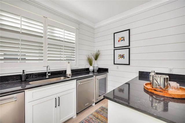 kitchen with white cabinetry, stainless steel dishwasher, wooden walls, and sink