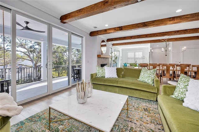 living room with beamed ceiling, light hardwood / wood-style floors, and ceiling fan with notable chandelier