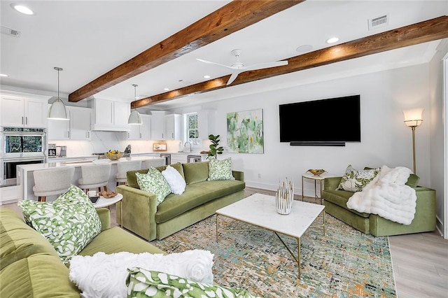 living room featuring beamed ceiling, light hardwood / wood-style floors, ceiling fan, and sink