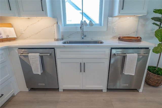 kitchen featuring white cabinets, light stone counters, stainless steel dishwasher, and sink