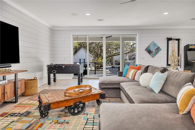 living room featuring wood walls, light wood-type flooring, and ornamental molding