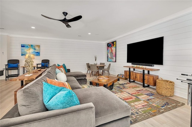 living room with ceiling fan, light wood-type flooring, ornamental molding, and wooden walls