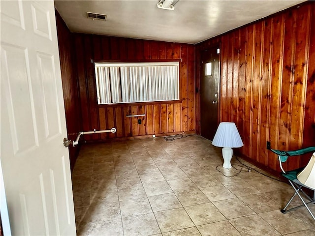empty room featuring tile patterned flooring, wood walls, and visible vents