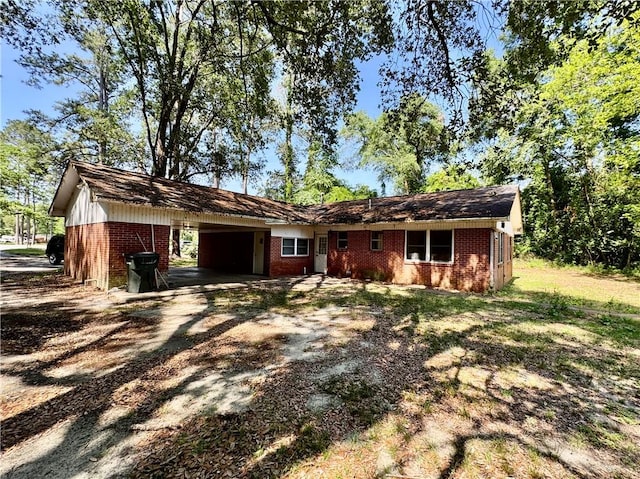ranch-style house featuring dirt driveway, an attached carport, and brick siding