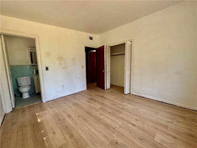 unfurnished bedroom featuring ensuite bathroom, a closet, wood finished floors, and visible vents