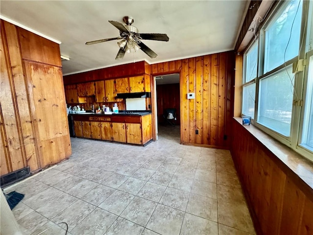 kitchen featuring brown cabinetry, wood walls, crown molding, dark countertops, and a ceiling fan