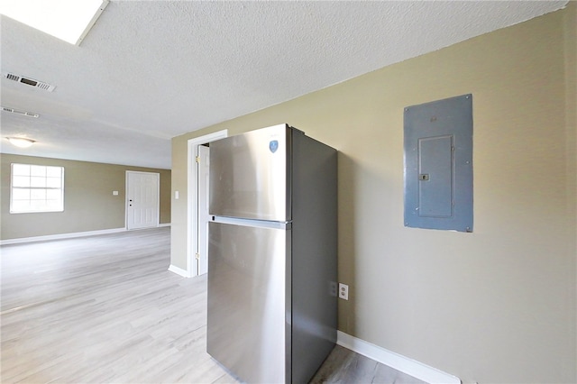 kitchen featuring a textured ceiling, light wood-style flooring, freestanding refrigerator, and electric panel