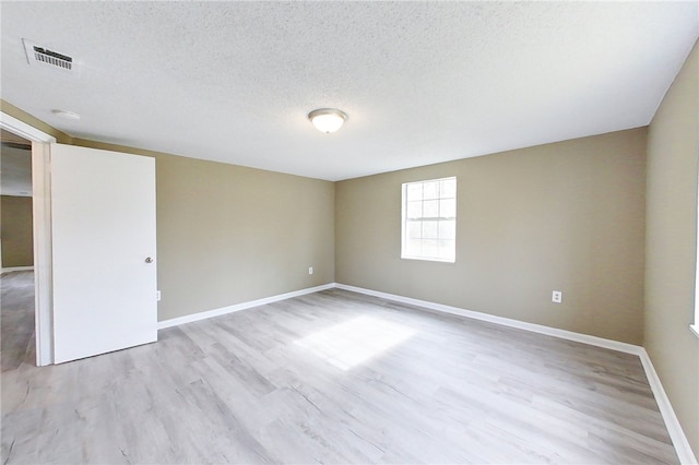 unfurnished room featuring a textured ceiling, light wood-style flooring, visible vents, and baseboards