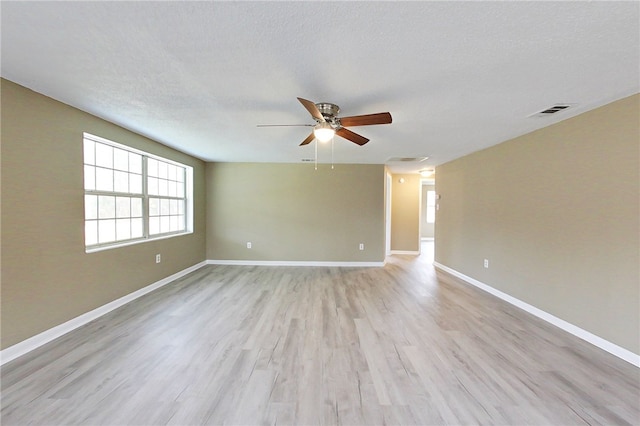 spare room featuring a textured ceiling, light wood-style flooring, visible vents, and baseboards